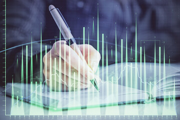 Double exposure of woman's hands making notes with forex graph hologram. Concept technical analysis.
