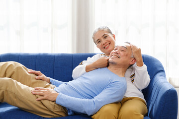 Portrait of happy Asian senior couple living together, hug, touching and embracing with a smile on the sofa in the living room. Retirement living together at home.