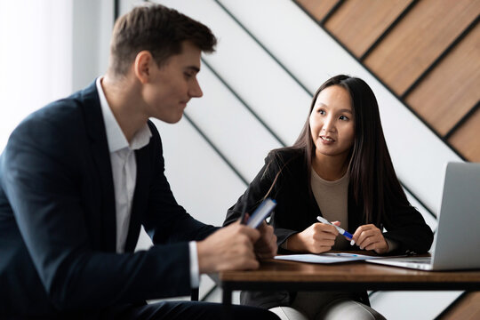 caucasian male candidate at an interview in the office answers questions of a female leader of Asian appearance