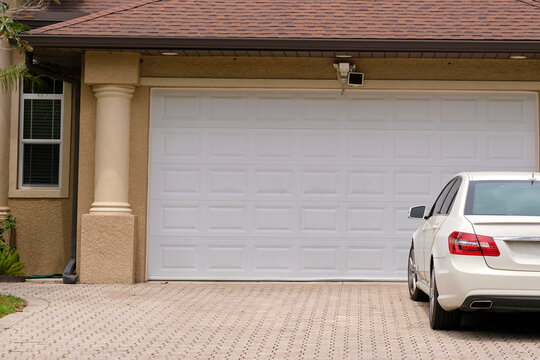 Vehicle parked in front of wide garage double door on paved driveway of typical contemporary american home