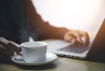 Man working in front of a laptop with hot coffee with smoke and steam	
