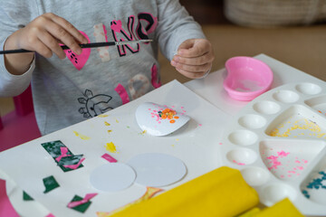 little child makes decorations from colored paper with glue and scissors and paint brush top view...