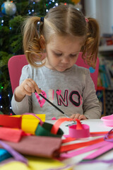 a little girl makes and decorates  decorations with colored paper and with sparkles