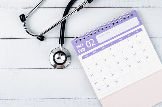 The Pink February 2023 desk calendar and stethoscope medical on wooden background, schedule to check up healthy concepts.
