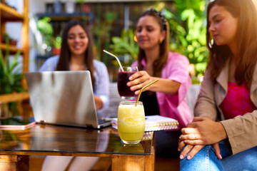 three young latin women sitting working with a laptop in a cafe out of focus, drinking juice