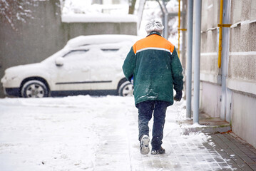 Worker with salt bucket spread salt mixture on walkway near residential building. Janitor melt snow spreading melting reagents, prevent slipping on road after snowfall. Janitor spread sand