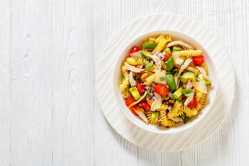 Healthy Chicken Pasta Salad with Avocado, Tomato, and olive oil and vinegar dressing in white bowl on white wood table,  horizontal view from above, flat lay﻿, free space