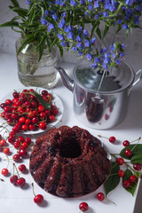 Chocolate cake with sweet cherry, vintage kettle and bouquet of blue flowers on white background..