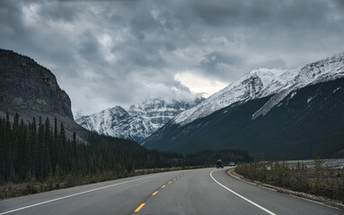 Road trip with car driving on highway with rocky mountains and gloomy sky in Banff national park