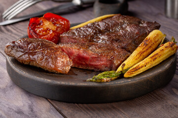 Roasted Top Blade beef steak with grilled vegetables  in wooden plate.