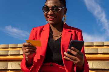 Happy black woman with short hair making payment via smartphone with credit card