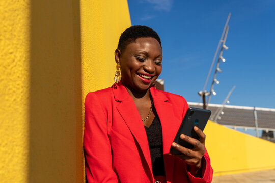 Cheerful black woman smiling while chatting on smartphone on street