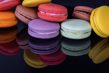 Lots of colorful macaroons on black background with reflection. Traditional french dessert