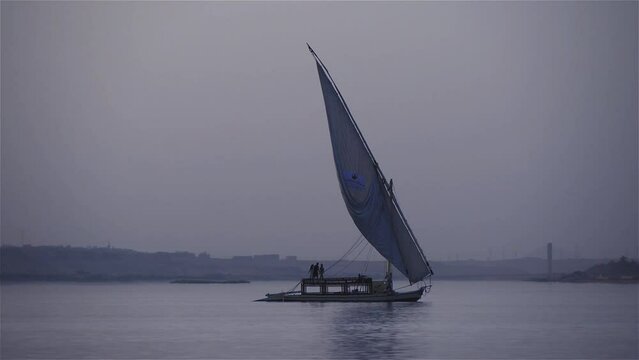 A Small Vintage Wooden Sailboat Sails On A Large River Early At Dawn. Filmed On River Nile in Egypt.