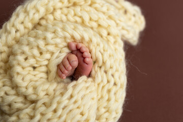 small legs of a newborn on a yellow background. knitted scarf yoke