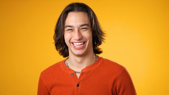 Portrait of smiling laughing, happy, handsome Hispanic gender fluid young man 20s wearing orange casual shirt isolated on yellow color background in studio. Sincere emotions lifestyle concept.