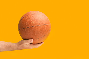 Mano de hombre sosteniendo una pelota de baloncesto sobre un fondo amarillo brillante liso y...