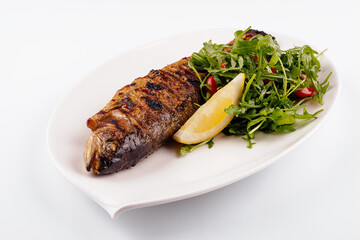 Grilled sea bream fish, lemon, arugula on white plate