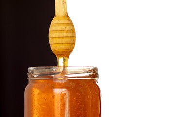 honey from the spoon drains into the jar. Spoon for honey. Honey on a black and white background