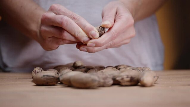 A woman approaches the table on which the pecans are lying and peels them from the shell with her hands.