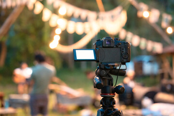 Camera recording standing on tripod with defocused illuminated live music concert event and camping