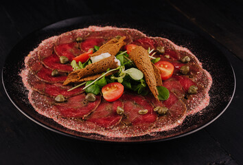 Beef carpaccio with capers on black plate