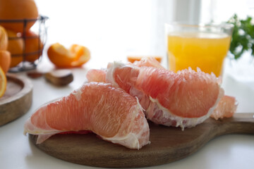 Pomelo in a cut on a wooden stand near a glass of freshly squeezed juice and oranges