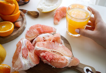 Pomelo in a cut on a wooden stand near a glass of freshly squeezed juice and oranges
