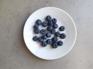 White dish of lush blueberries against grey neutral coloured background