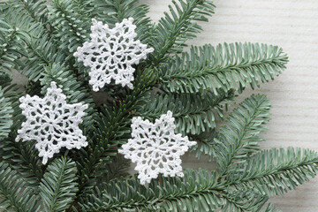 Handmade cotton Christmas white crocheted snowflake close up and fir tree branches top view