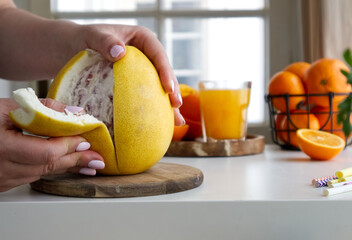  Female hands clean a pomelo standing on a wooden stand and near oranges and juice