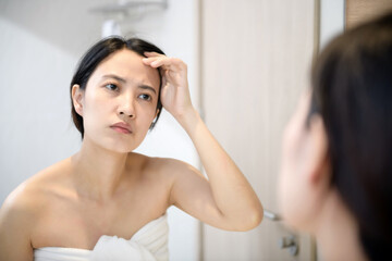 Fototapeta premium Problem skin. Concerned young asian women popping pimple on cheek while standing near mirror in bathroom. young asian women with acne