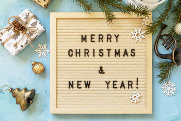 Merry Christmas and Happy Holidays greeting cards New Year. Merry Christmas lettering on letter board, gifts boxs and gold  decorations on a blue background. View from above.