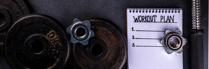 Fitness or bodybuilding background. Old hard iron dumbbells, small colorful dumbbells,  notepad with workout plan list. Back to gym concept, weight lifting sport flat lay top view copy space  