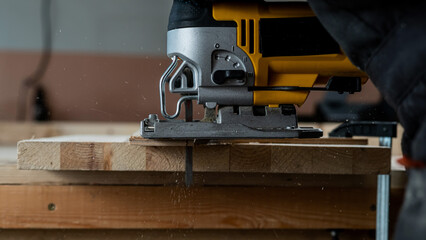 Close-up of a man cutting a wooden plank with an electric jigsaw in a workshop.