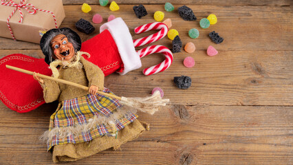 The funny witch Befana and red stocking with sweet coal and candy on rustic wooden background. Italian Epiphany day tradition, top view, flat lay, greeting card, web banner