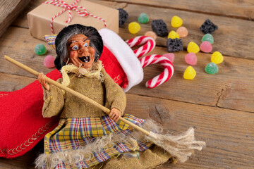 The witch Befana and red stocking with sweet coal and candy on rustic wooden background. Italian Epiphany day tradition, top view, flat lay, greeting card