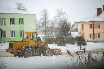 snow plow tractor rides on city road in snowfall.