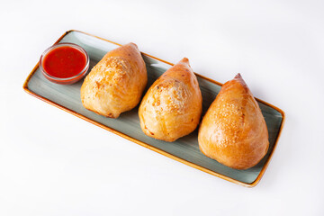 three samsa with tomato sauce on a white background
