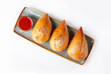 three samsa with tomato sauce on a white background