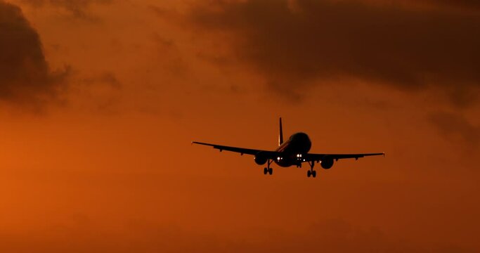Plane flies through the dark orange sunset sky and lands at the airport. Cancellation of covid restrictions and opening of international borders. Free tourism and airline travel after the lockdown.