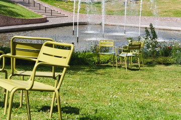 Movable chairs in the public space of a modern city. Free green steel chairs in the park on the lawn next to the pond. Concept of modern urban landscape design, design public spaces.