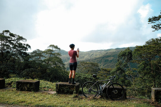 A young female cyclist is taking photos with her mobile device in the mountains.
