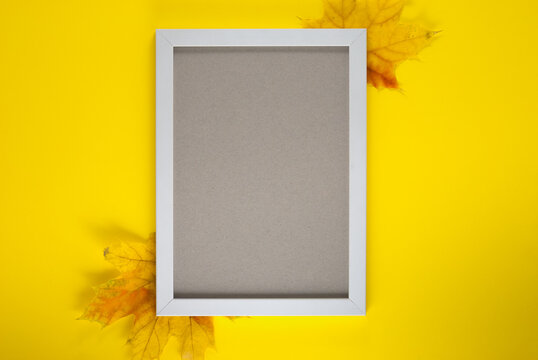 Autumn composition. Photo frame, leaves on yellow background. Flat lay, top view, copy space