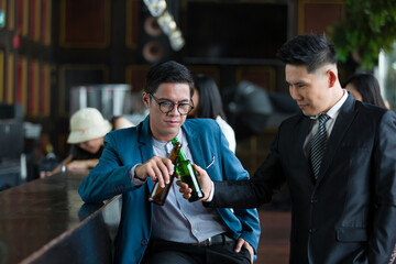 Two Asian business man or partnership holding bottles of beer and drinking discussing project work in the office work space