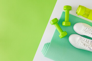 Fitness concept. Flat lay composition of dumbbells exercise mat bottle of water sports shoes on white and green background with copy space. Minimal athletics accessories idea. - Powered by Adobe