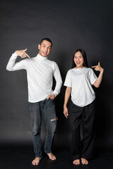 Young energetic couple wearing white blank shirt doing a pose while smiling happily with a black background