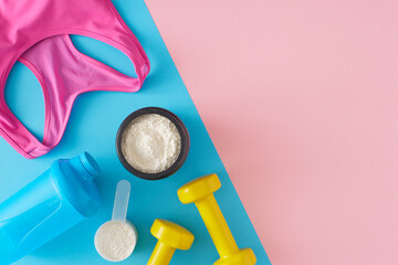 Fitness diet concept. Top view photo of whey protein in jar with shaker, pink sports top and dumbbells on pastel pink and blue background. Flat lay with copy space.