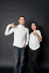 Young energetic couple wearing white blank shirt doing a pose while smiling happily with a black background