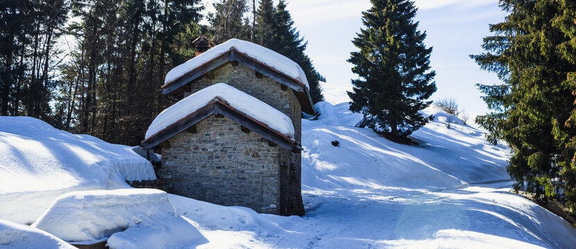 Italian mountain winter landscape. Panoramic view of the small stone houses in the woods. Shadow play on the snow. Combai, Italy